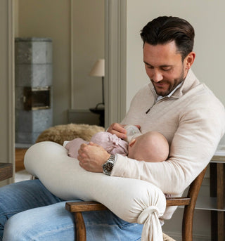 A dad feeding his baby using a nursing pillow