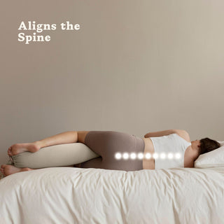 Person lying on a bed with a bbhugme pregnancy pillow 