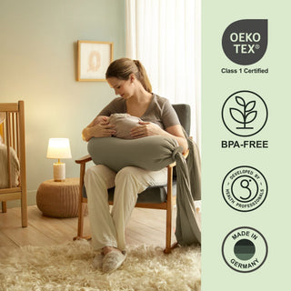 Woman holding a baby in a green cushioned chair with Oeko-Tex and BPA-Free certification icons on the right bbhugme pregnancy pillow